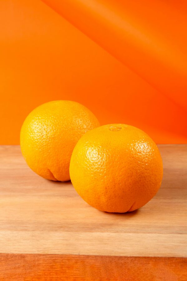 pexels-photo-30925639-30925639 Two fresh oranges on a wooden surface with vibrant orange background, showcasing their bright, juicy texture.