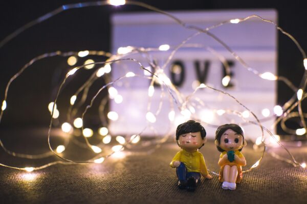 Adorable couple figurines surrounded by warm glowing fairy lights with a 'LOVE' sign.
